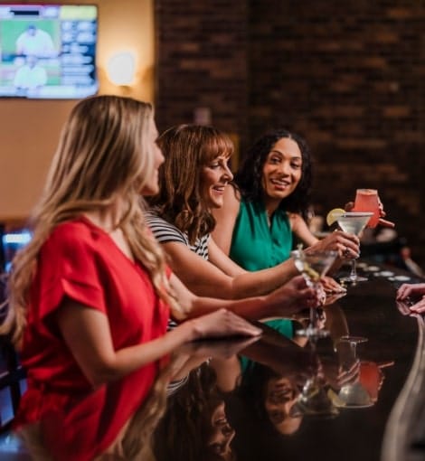 women sitting at bar holding cocktails